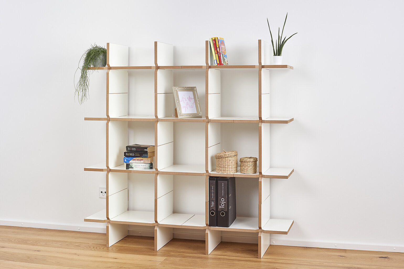 Mittelhohes Regal „solo“ von Tojo in Weiß mit naturbelassener Kante, bestückt mit Pflanzen, Büchern und Ordnern – freistehend vor weißer Wand im Wohn- oder Arbeitsraum