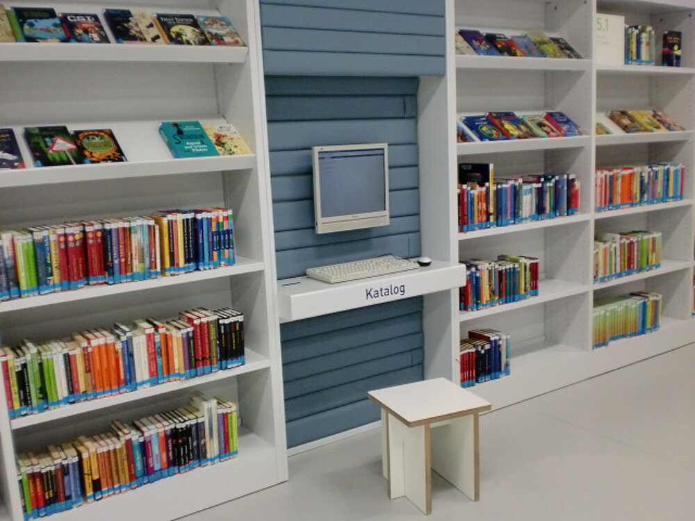 Ein Tojo Regalsystem in einem hellen Raum, das Bücher organisiert und einen praktischen Arbeitsplatz mit einem kleinen Tisch bietet.