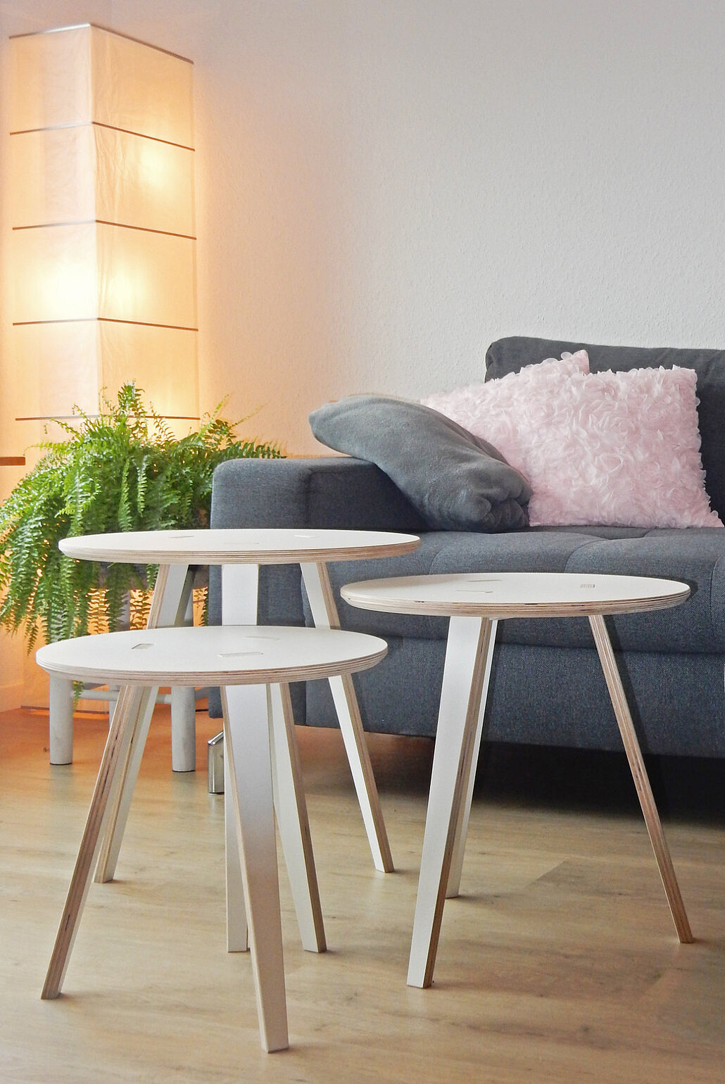 Zwei runde Tojo-Tische aus Holz vor einem grauen Sofa im gemütlich eingerichteten Wohnzimmer mit Pflanzen und Beleuchtung