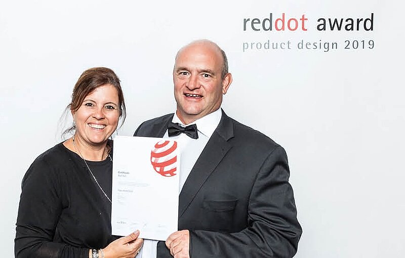 Mann und Frau in eleganter Kleidung mit Red Dot Award Urkunde vor Fotowand