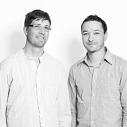 Schwarz-weißes Porträt des Designteams floid – zwei Männer in gemusterten Hemden vor hellem Hintergrund