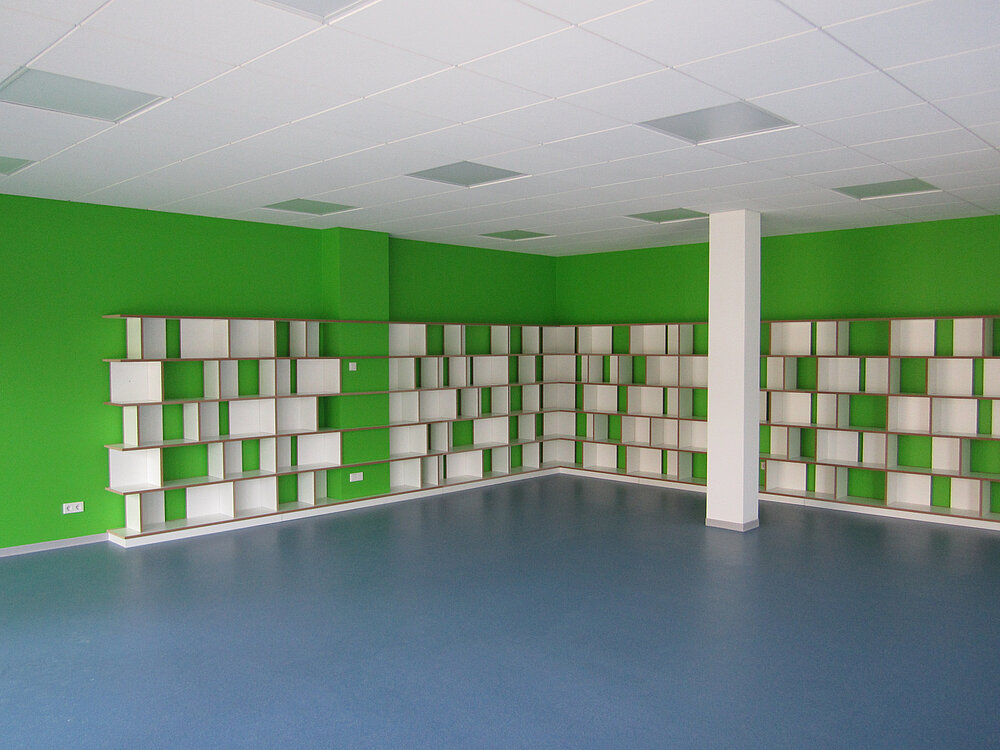 Moderne Regalsysteme von Tojo, die an grünen Wänden aufgestellt sind, bieten viel Stauraum und eine flexible Gestaltung des Raums, ideal für Bücher oder andere Aufbewahrungslösungen.