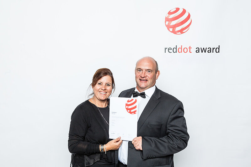 Preisträgerin und Preisträger bei der Red Dot Award Verleihung, halten gemeinsam die Urkunde vor dem offiziellen Logo