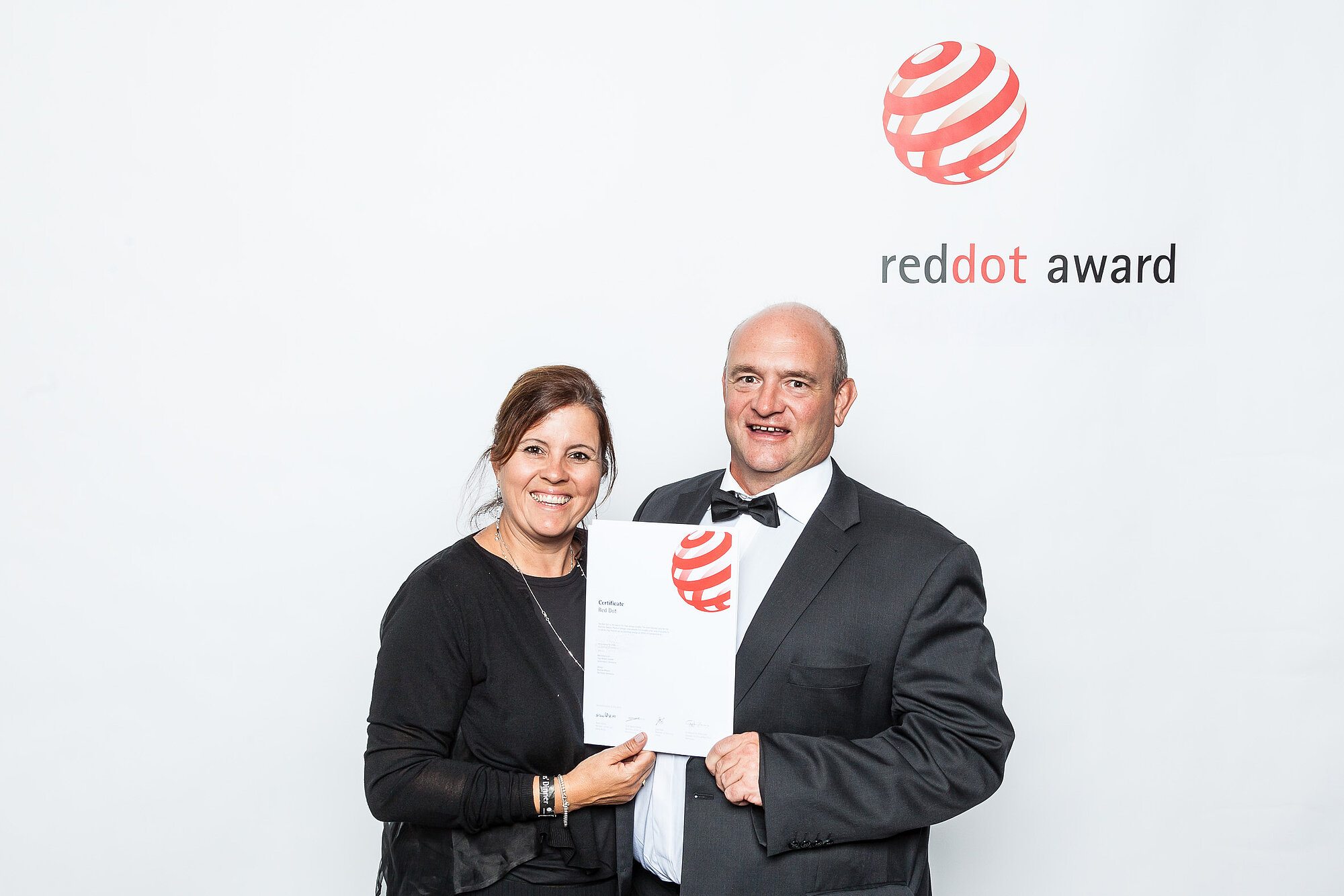 Preisträgerin und Preisträger bei der Red Dot Award Verleihung, halten gemeinsam die Urkunde vor dem offiziellen Logo