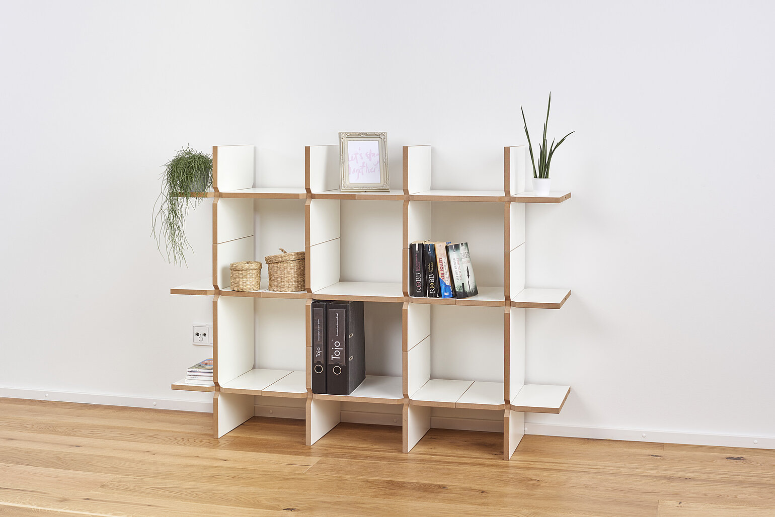Kleines Regal „solo“ von Tojo in Weiß mit naturbelassenem Holzrahmen, aufgestellt vor weißer Wand und dekoriert mit Pflanzen, Büchern und Ordnern