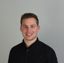 Porträt von Produktdesigner Demmler vor grauem Hintergrund, freundlich lächelnd in dunklem Hemd