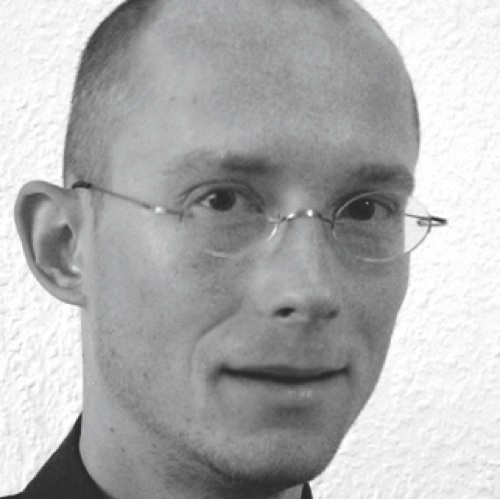 Schwarz-weißes Porträt von Produktdesigner Hammer mit Brille und ruhigem Blick, vor heller Wandstruktur
