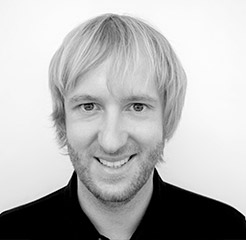 Schwarz-weißes Porträt von Produktdesigner Katter mit hellem Haar und freundlichem Lächeln vor neutralem Hintergrund