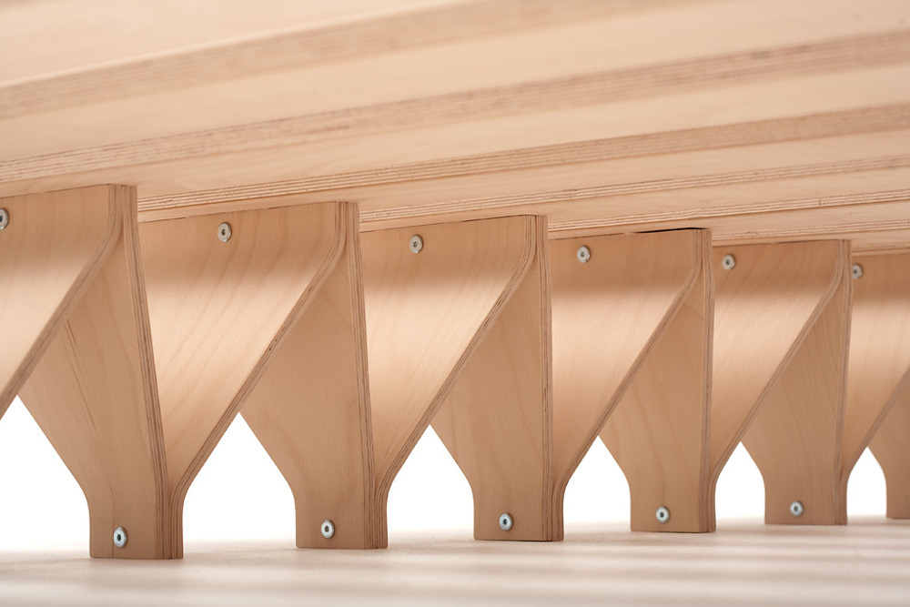 Blick unter ein Holzgestell mit mehrfach wiederholten, schrägen Stützverbindungen aus hellem Schichtholz – klare Linien und stabiles Design