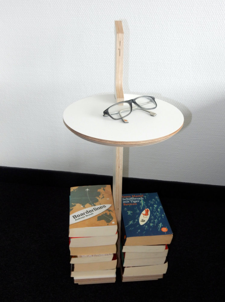 Tojo Lesestelle, ein minimalistisches Kleinmöbel mit Tischplatte auf einem Bücherstapel – ideal für Bücher und Brillen.