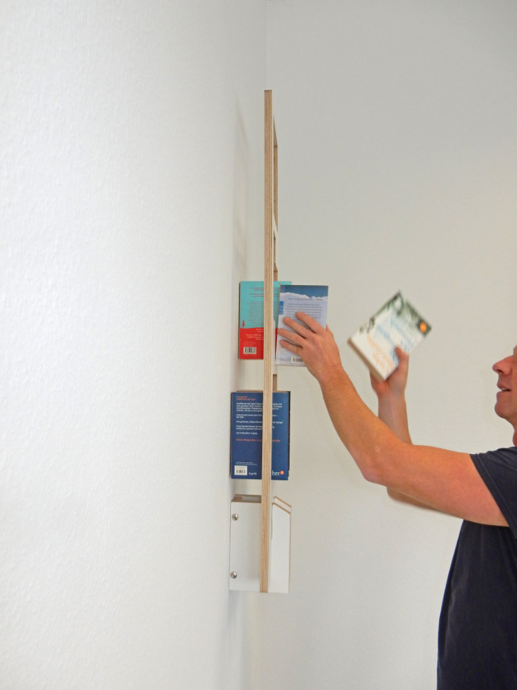 Tojo Lesestoff Wandregal als Bücherregal, das von einer Person mit Büchern bestückt wird