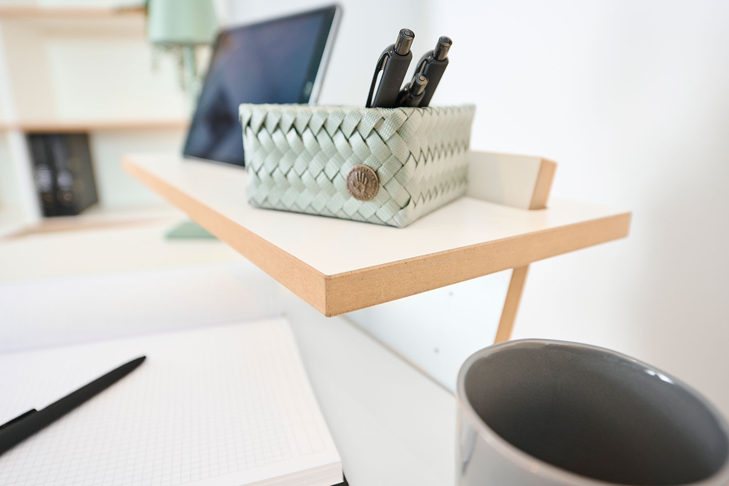 Detailaufnahme des Tojo Pults mit einem Stifteköcher und einer Tasse auf der Ablagefläche. Ein praktisches, minimalistisches Design, das den modernen Arbeitsplatz ergänzt.