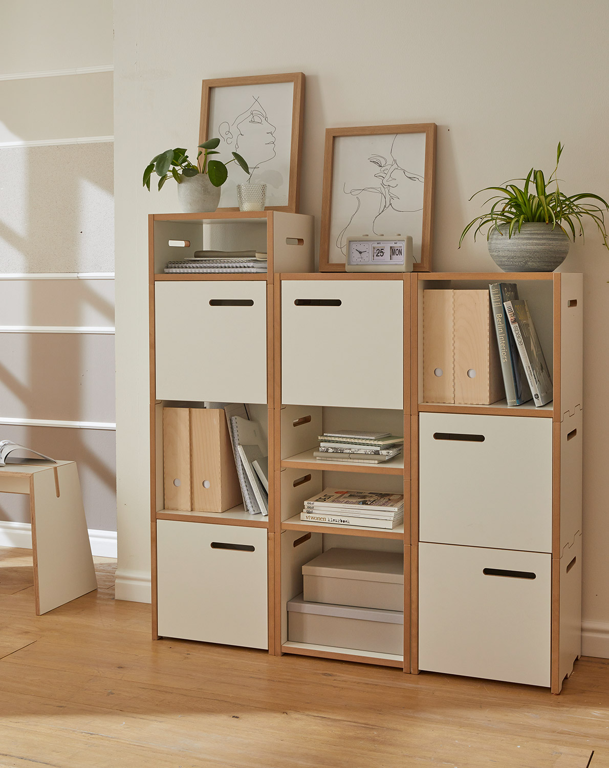Regalkombination „halbstark“ von Tojo mit weißen Modulen und Holzrahmen, arrangiert mit Büchern, Körben und Deko in einem gemütlich eingerichteten Raum