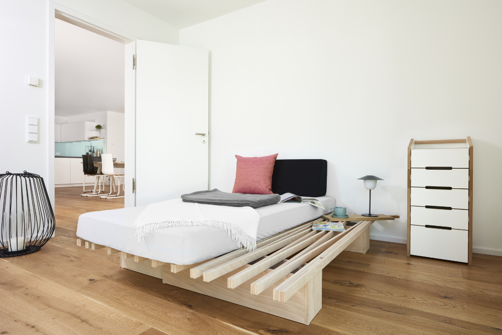 Tojo Schrank „cargo“ mit vier Schubladen neben einem Bett im modernen Schlafzimmer – weißes Möbel mit naturbelassener Kante auf Holzfußboden