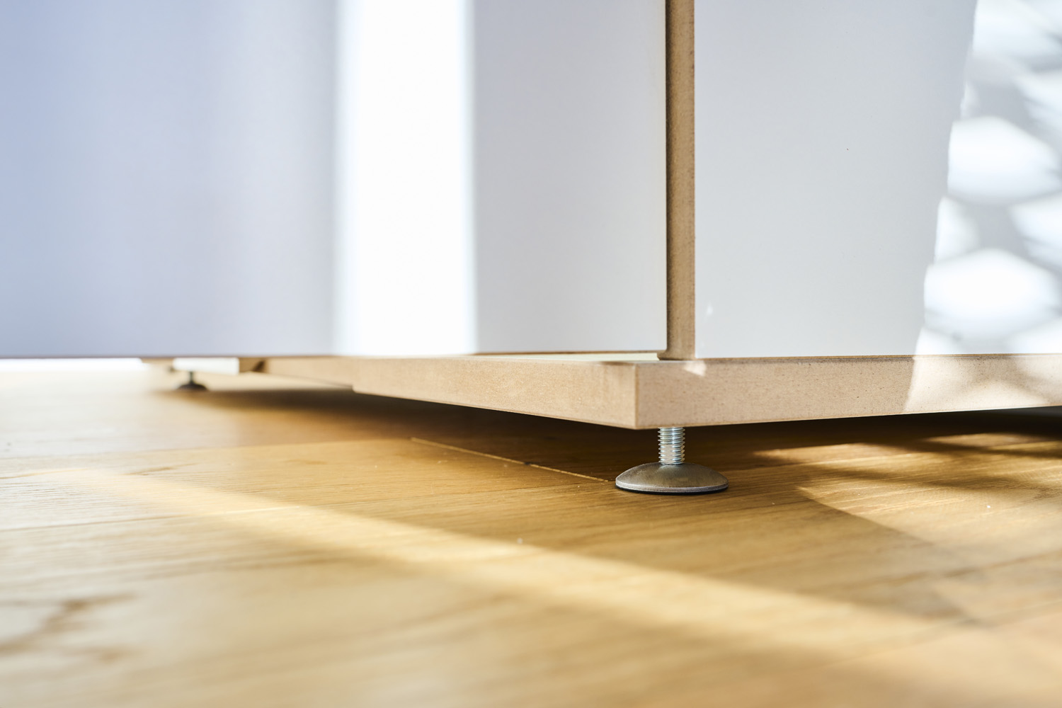 Nahaufnahme des verstellbaren Sockelfußes am Tojo Schrank „stau“ mit Fokus auf die Bodenfreiheit und Materialstruktur
