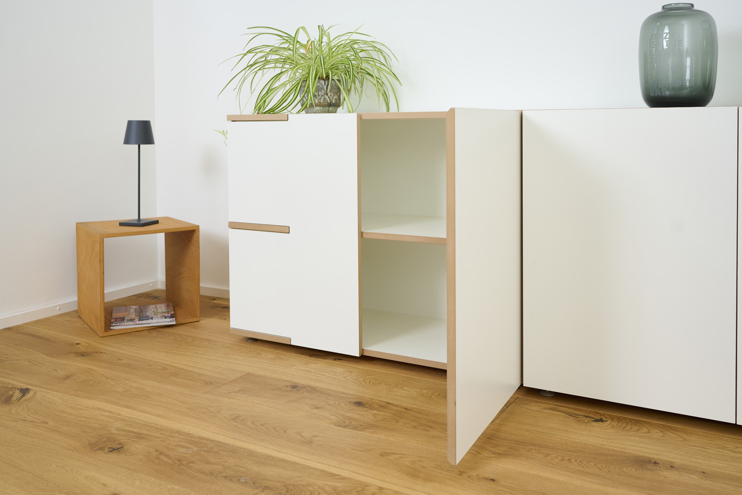Geöffneter weißer Schrank Tojo stau mit Einlegeboden, daneben eine Holzablage mit Lampe und Pflanze auf dem Schrank