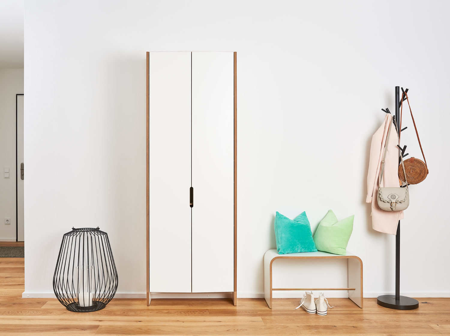 Minimalistische Sitzbank sit von Tojo aus weiß beschichtetem Holz mit sichtbarer Multiplexkante, platziert in einem Flur neben Kissen, Garderobe und Deko