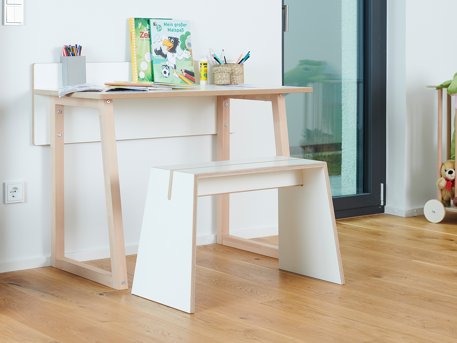 Tojo stubenhocker vor einem Kinderschreibtisch mit Spielzeug und Büchern, in einer hellen Wohnumgebung mit Holzfußboden