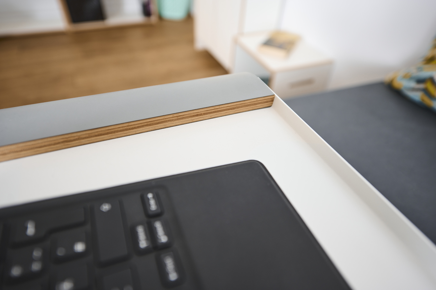 Nahaufnahme der Tischkante des Tojo praktisch mit sichtbarer Schichtholzkante und einem Teil einer Tastatur auf der Tischplatte
