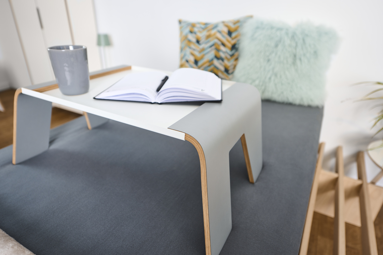 Tojo Tisch praktisch als Beistelltisch auf einem Bett mit Kissen, Buch und Becher dekoriert