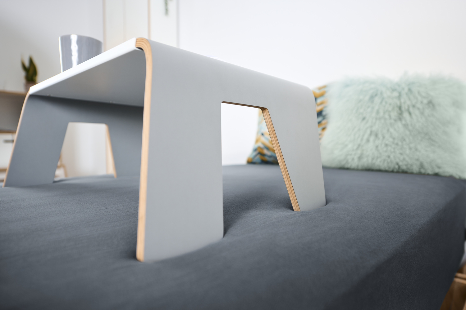 Tojo Tisch praktisch in Seitenansicht auf einem Bett, mit geschwungenem Design und Becher