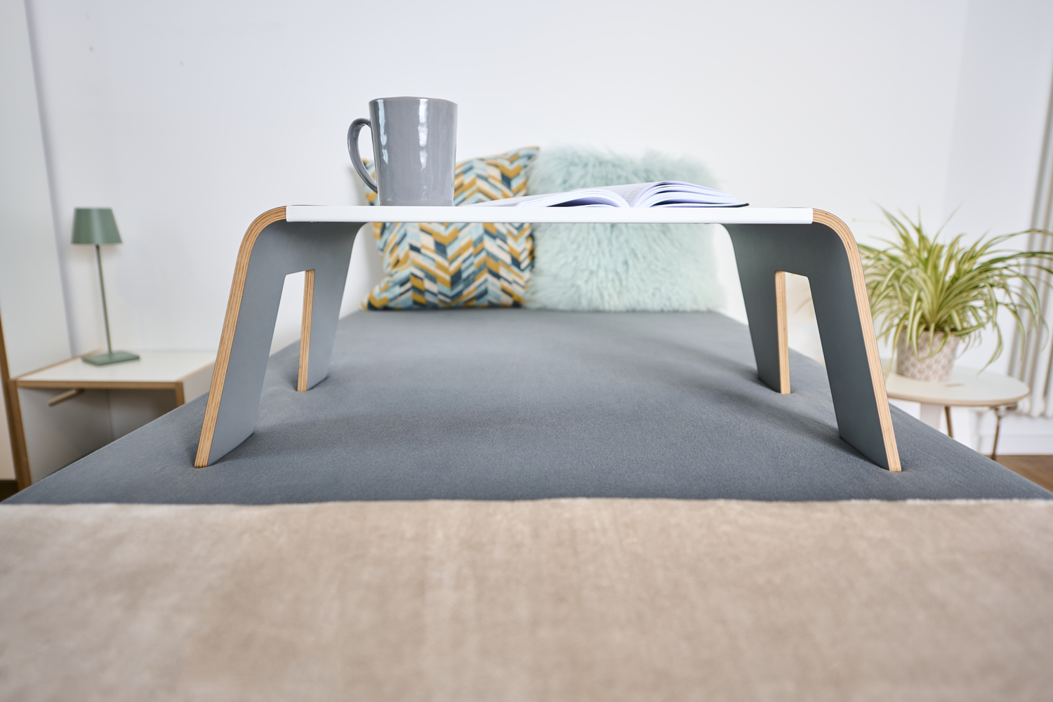 Tojo Tisch praktisch auf einem Bett platziert, mit Lampe, Pflanzen und Kissen im Hintergrund
