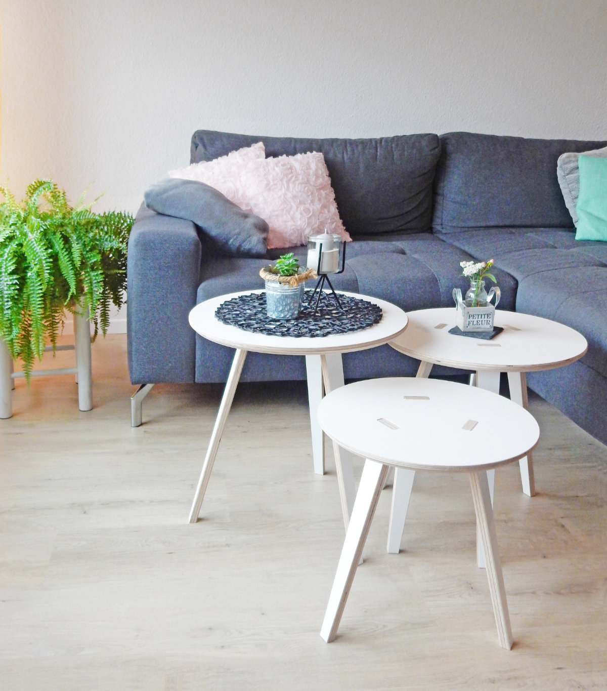 Drei runde Beistelltische von Tojo in einem modernen Wohnzimmer vor einem grauen Sofa mit farbigen Kissen und grüner Zimmerpflanze