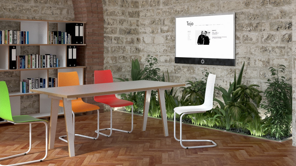 Tojo Tisch steck in einem modernen Raum mit bunter Bestuhlung, Holzboden, Pflanzenwand und Bücherregal – ideal für Ess- oder Arbeitsbereiche