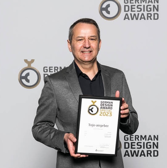  Mann im grauen Anzug mit Urkunde des German Design Award vor offizieller Fotowand